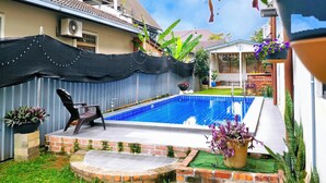 A backyard with a swimming pool, a covered patio area, and a garden with various plants. - Villa 223 (Bandar Baru Bangi)