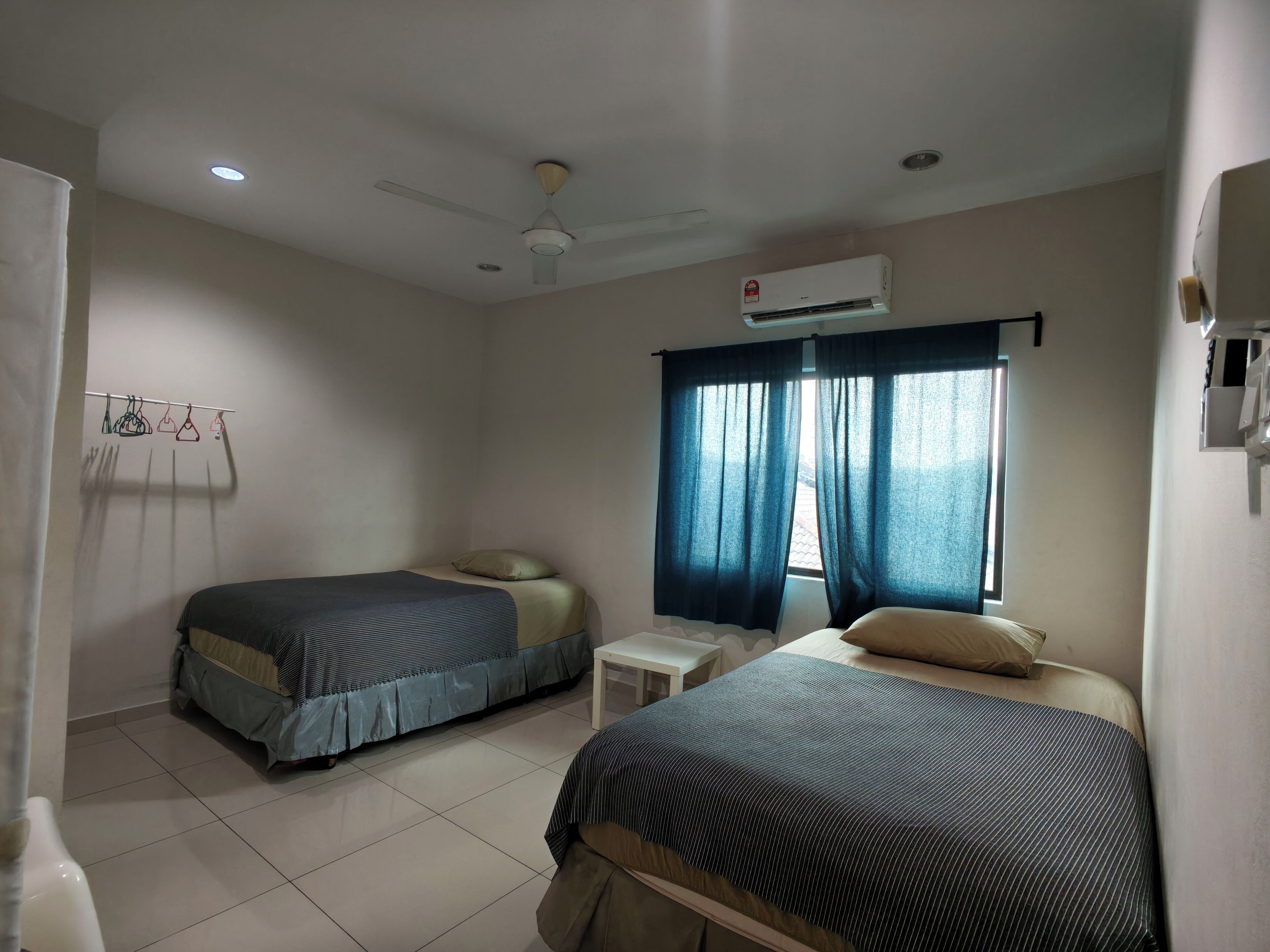 A room with two beds, a ceiling fan, an air conditioning unit, and a window with curtains.