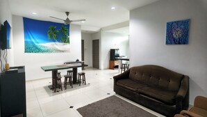 A modern living room with a brown sofa, a dining area with a table and chairs, a ceiling fan, and a painting of a beach scene. - Villa 223 (Bandar Baru Bangi)