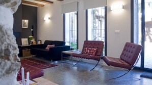 A modern living room with a dark sofa, a red armchair, and a coffee table. There are large windows and a stone wall in the background. - La Baranda (Chulilla)