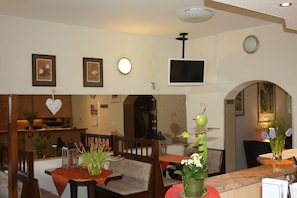 Un comedor con muebles de madera, un televisor montado en la pared y un florero sobre la encimera.