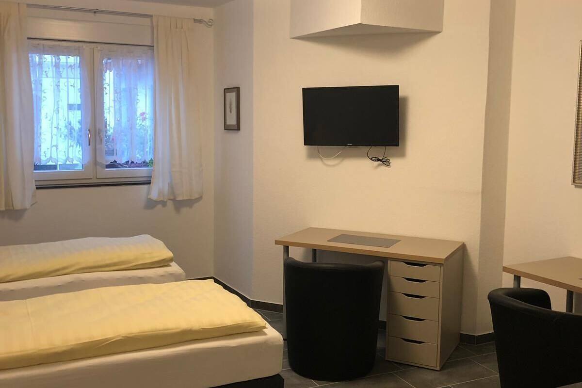 A bedroom with two beds, a desk, a chair, a TV, and a window with curtains.