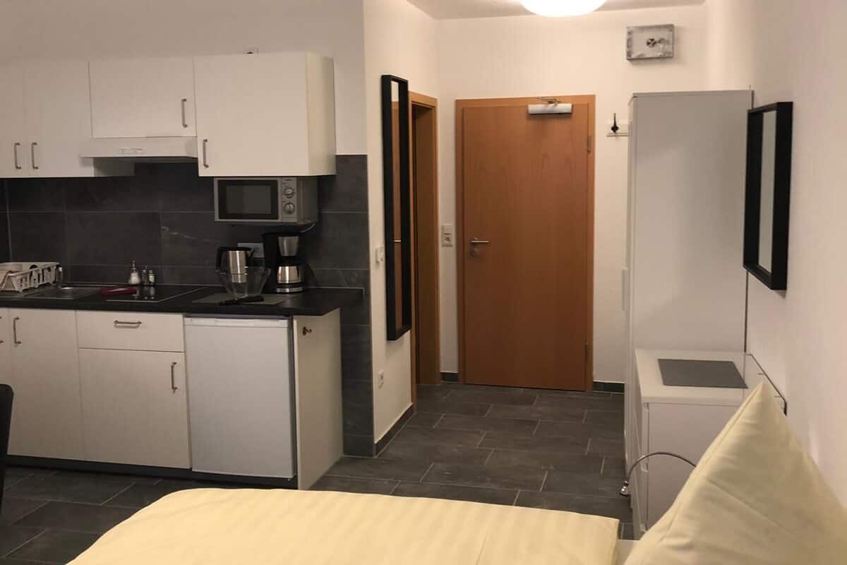 A compact room with a bed, a kitchenette, a door, and a small white cabinet.