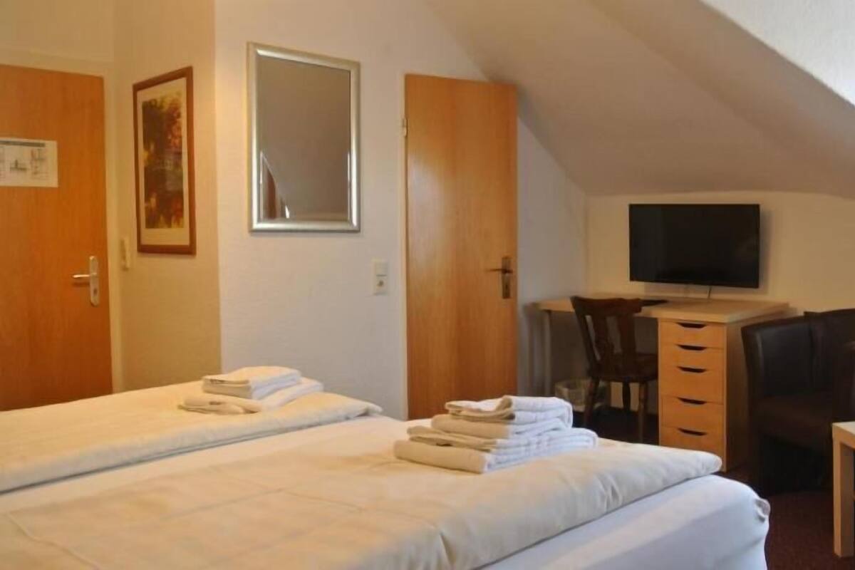 A hotel room with two beds, a desk with a TV, a chair, and a small table.