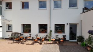 A courtyard with outdoor seating, potted plants, and a building facade with multiple windows. - Am Kamin (Duisburg)