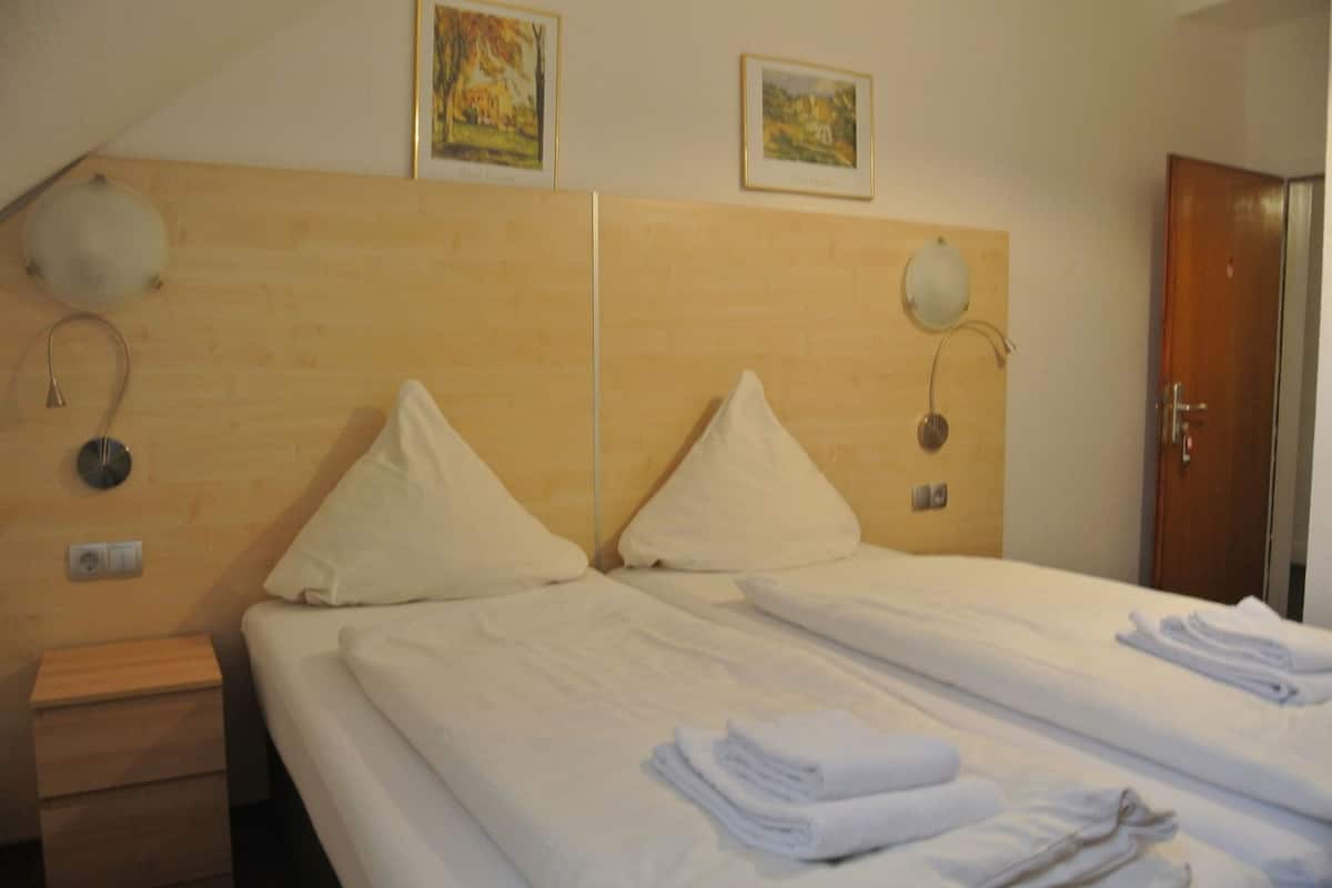 A hotel room with two beds, a wooden headboard, wall-mounted lamps, and framed pictures on the wall.