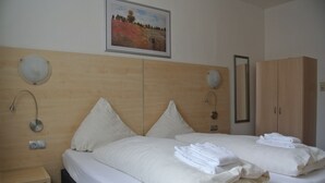 A hotel room with two beds, wooden headboards, a painting of a field, a mirror, and a wardrobe. - Am Kamin (Duisburg)
