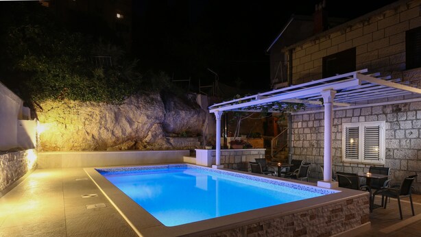 A swimming pool with a stone border, a pergola, and outdoor seating. - Guest House Kusalo (Dubrovnik)