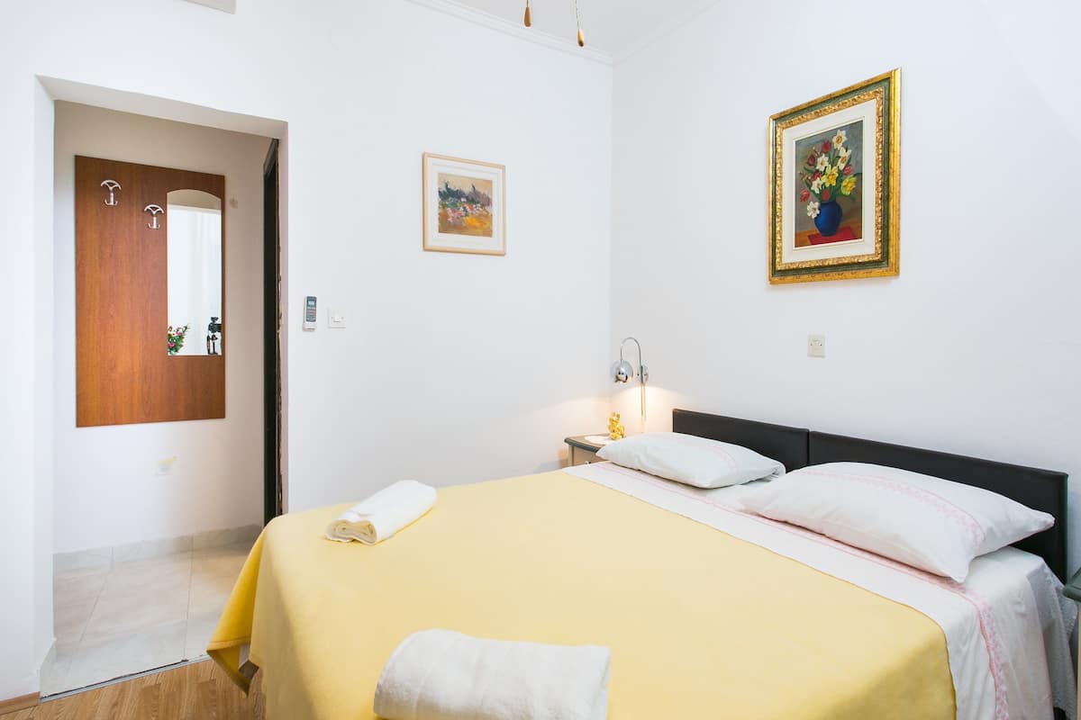 A hotel room with a bed, a nightstand, a lamp, a painting, and a door.