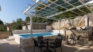 A pool area with a pergola, seating, and a stone wall. - Guest House Kusalo (Dubrovnik)
