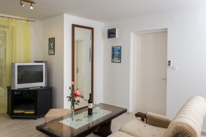 Ein Wohnzimmer mit Fernseher auf einem Schrank, einem Tisch mit Blumenvase und einer Couch.