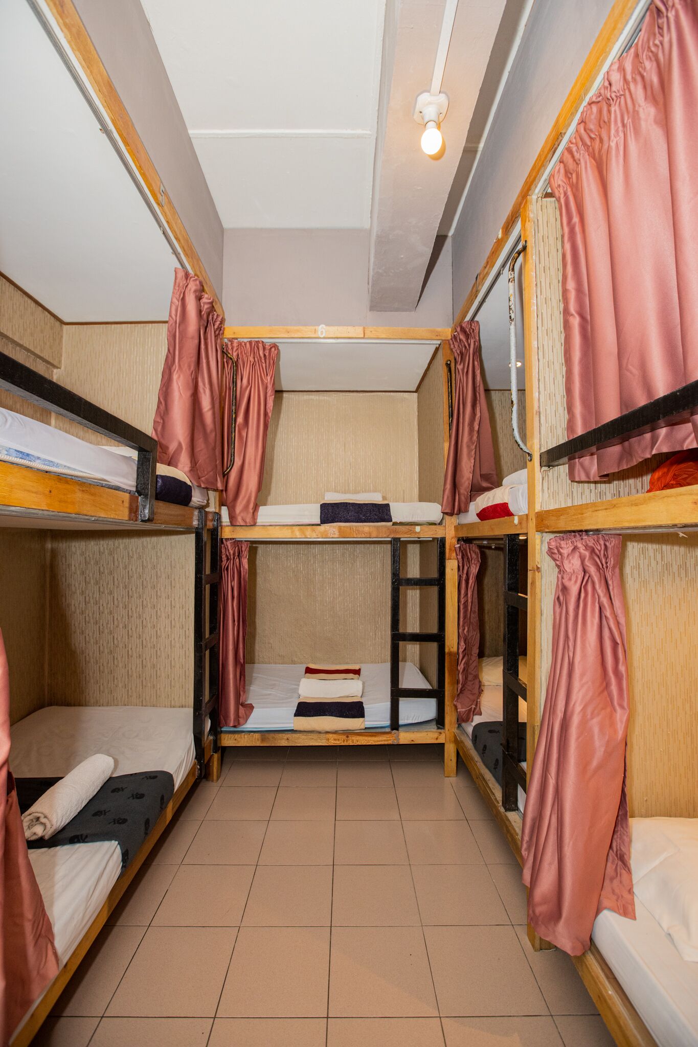 A dormitory room with bunk beds, a ceiling light, and a tiled floor.