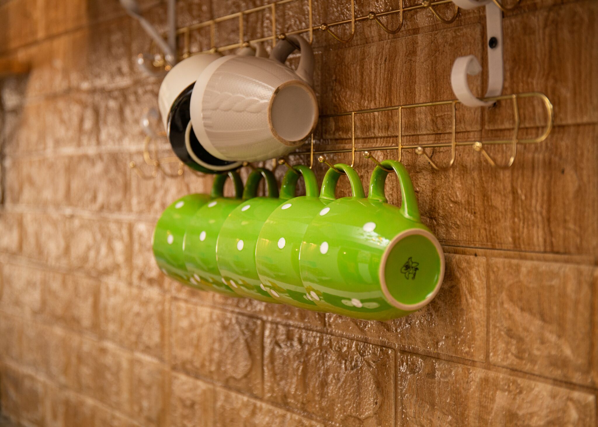 A wall-mounted rack holding several mugs and a green mug with white dots.