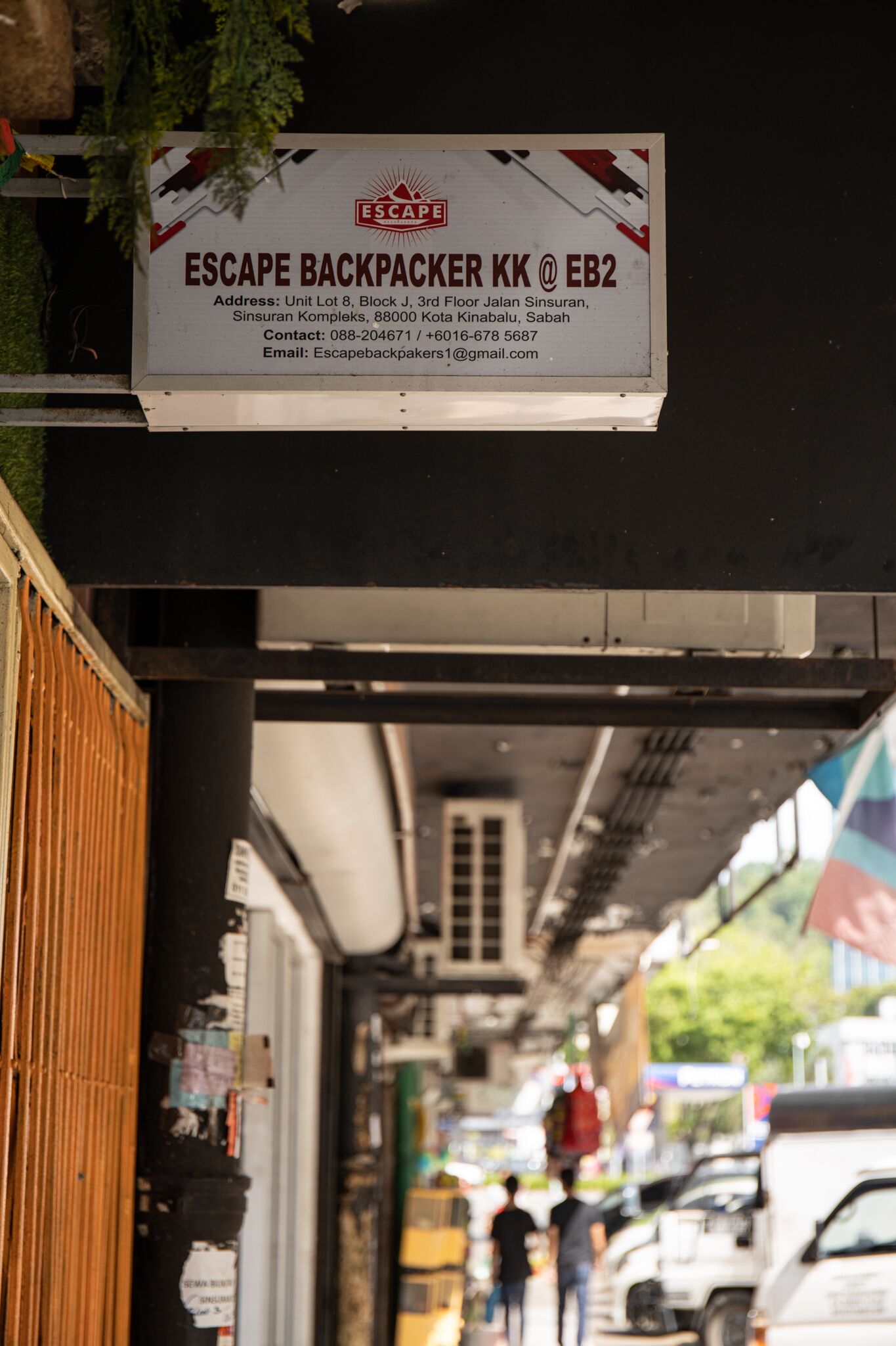 A sign for Escape Backpacker KK at EB2 with contact details and an address.