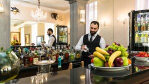 A bar area with a variety of bottles, a fruit bowl, and a person preparing a drink. - Hotel Caruso Old Town Prague (Prague)