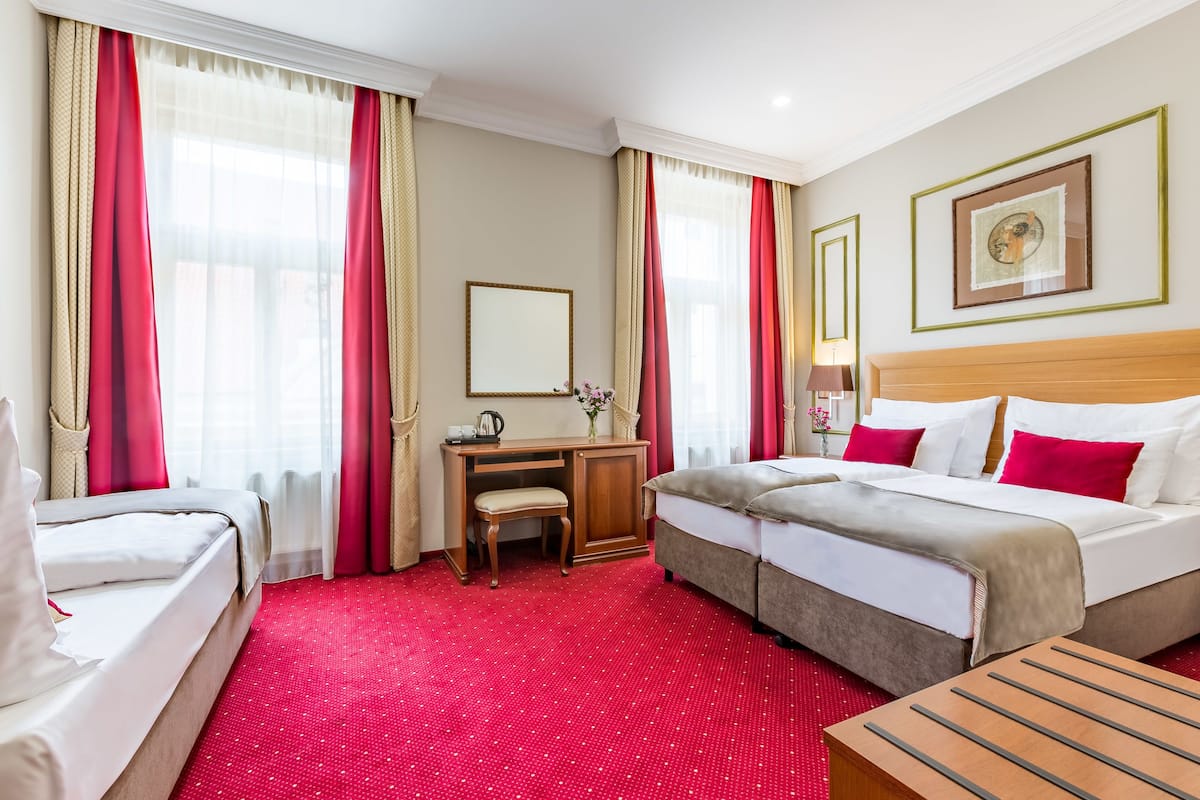 Una camera d'albergo con tappeto rosso, due letti, una scrivania con sedia e una testiera in legno.