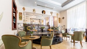 A well-lit, elegant dining area with green upholstered chairs, a marble floor, and a central bar area with a chandelier. - Hotel Caruso Old Town Prague (Prague)