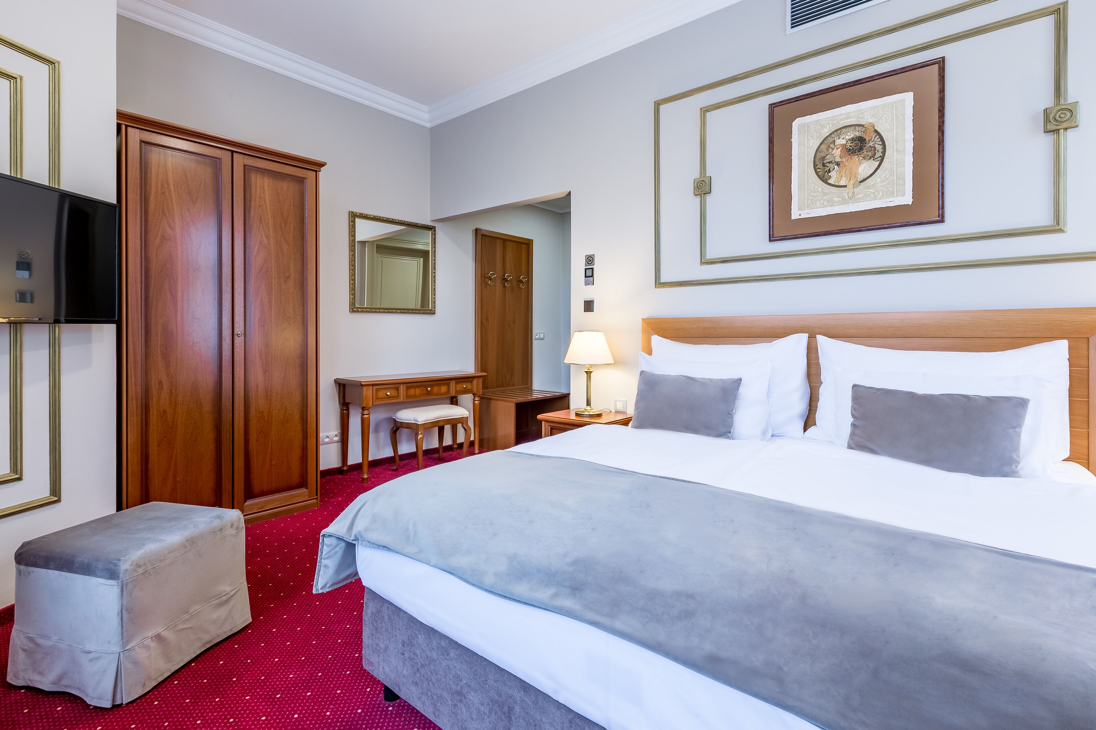 A hotel room with a large bed, a desk, a chair, a wardrobe, and a television.