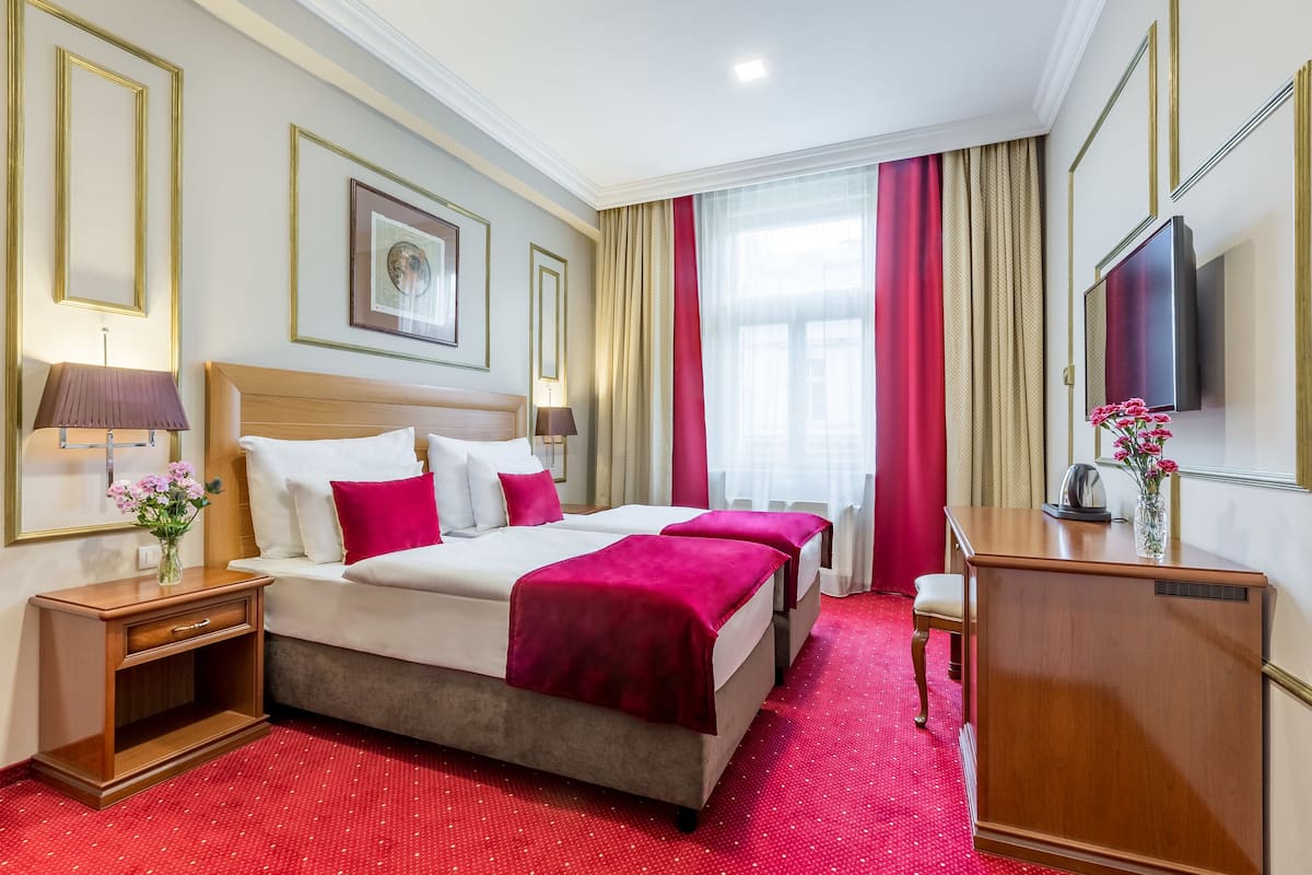 Una camera d'albergo con un letto grande, due comodini, una scrivania, un televisore e una finestra con tende.