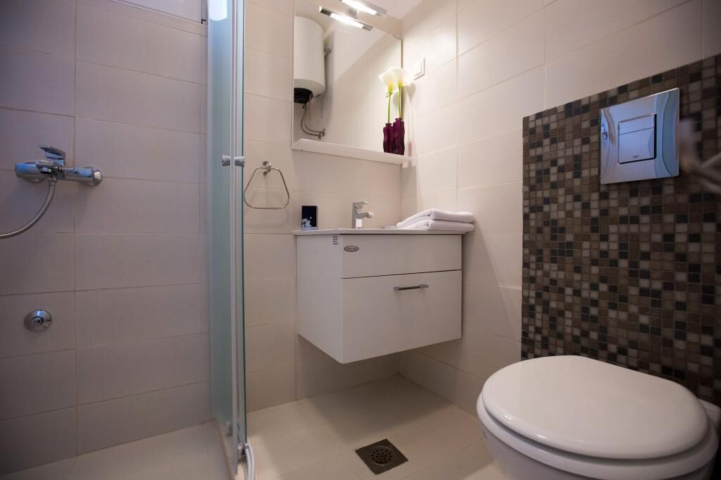 A modern bathroom with a glass shower enclosure, a white sink with a mirror above, and a toilet with a mosaic tile backsplash.