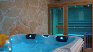 Un jacuzzi con dos chorros, una pared de piedra y una puerta de madera con panel de vidrio.