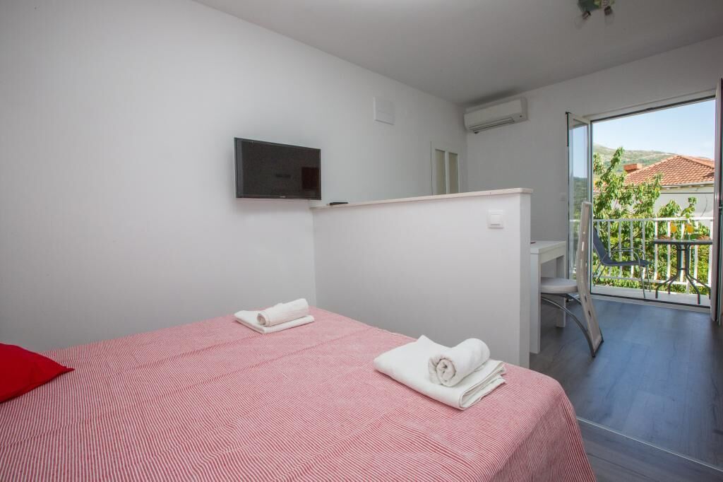 Une chambre d’hôtel avec deux lits, un téléviseur fixé au mur et un balcon offrant une vue sur la verdure et les bâtiments.