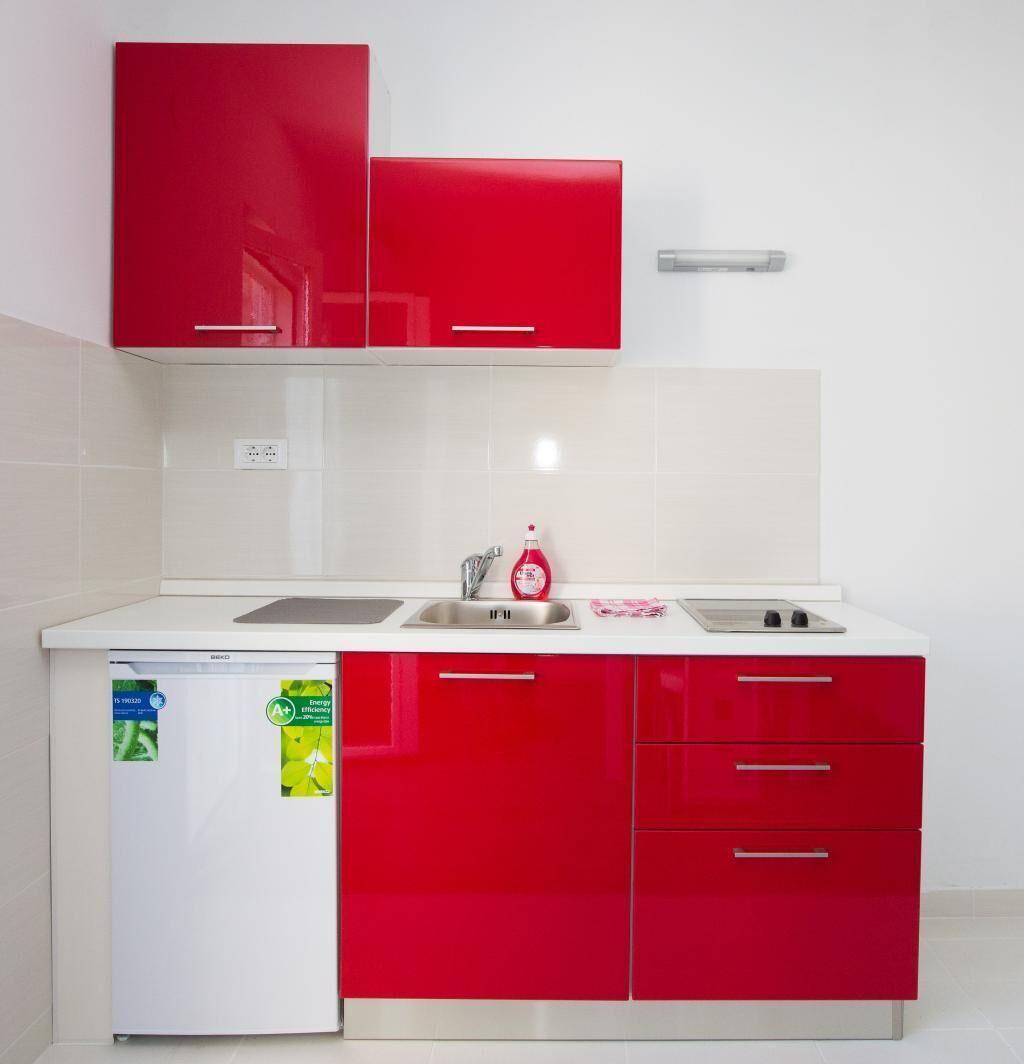 A kitchen with red cabinets, a white countertop, a built-in dishwasher, and a stainless steel sink.