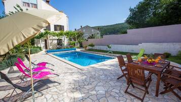 Un patio in pietra con piscina, area salotto esterna e una zona coperta con ombrelloni.