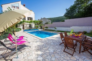 A stone patio with a swimming pool, outdoor seating, and a covered area with umbrellas. - Apartments Villa Roza (Dubrovnik)