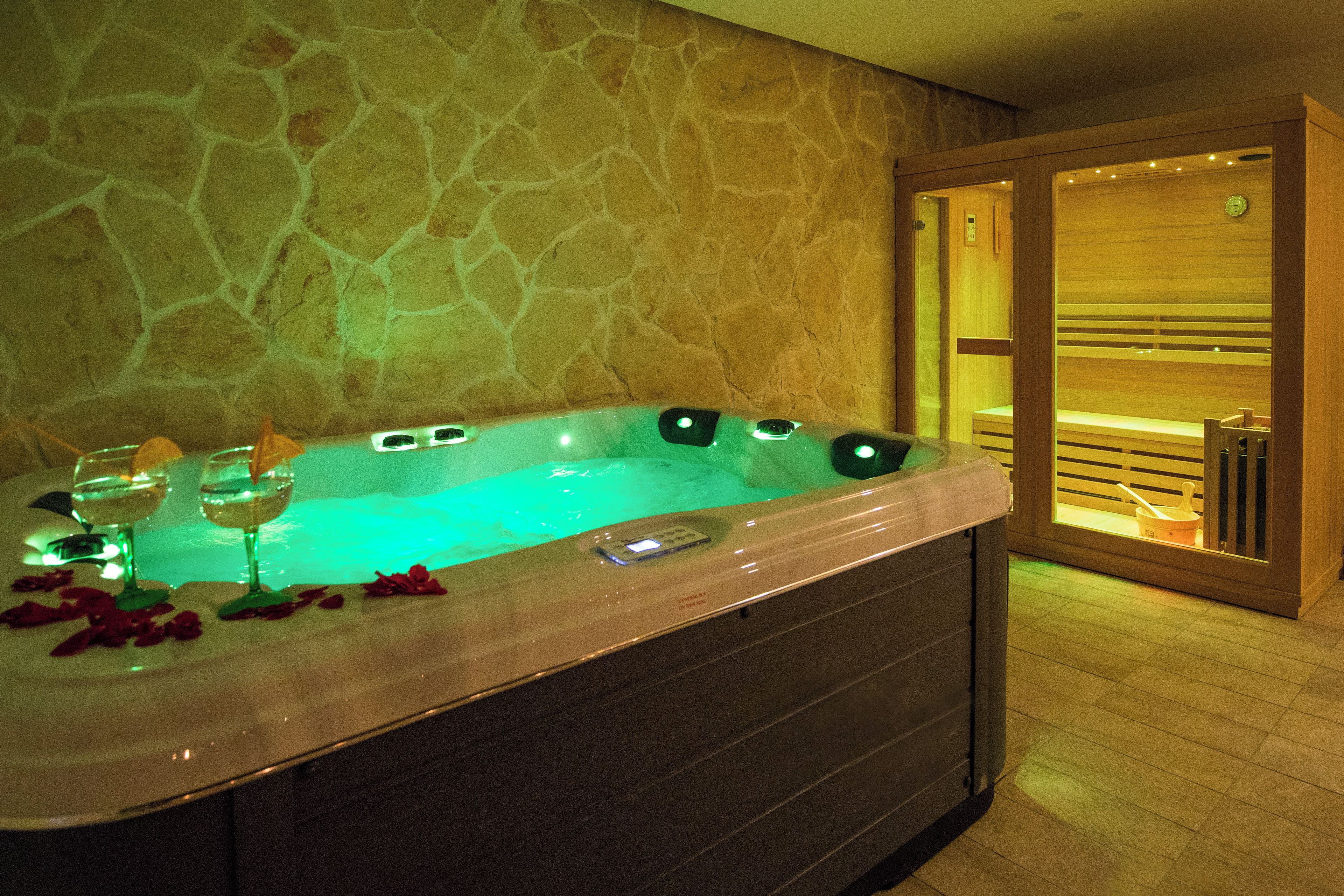 A spa area with a hot tub, two glasses of wine, and rose petals on the edge.