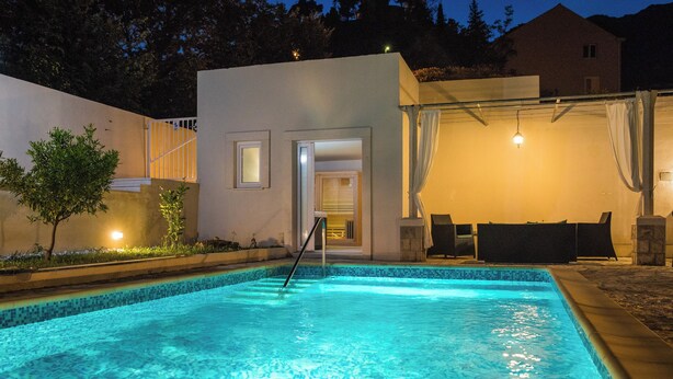 Una piscina con borde de azulejos, un área de descanso cubierta y un edificio con una puerta que da a un espacio interior.