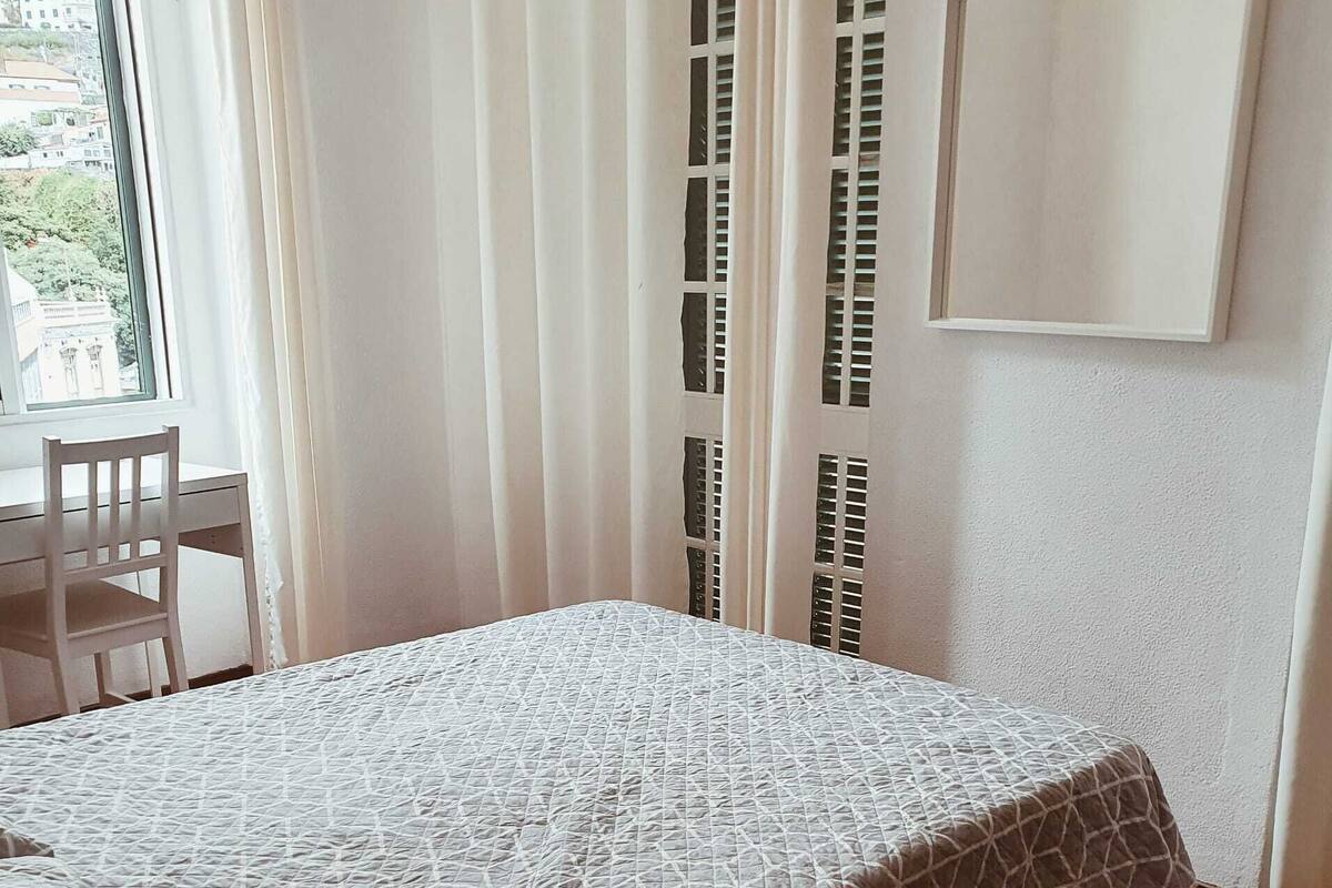 A room with a bed, a chair, a window, and a wall-mounted TV.