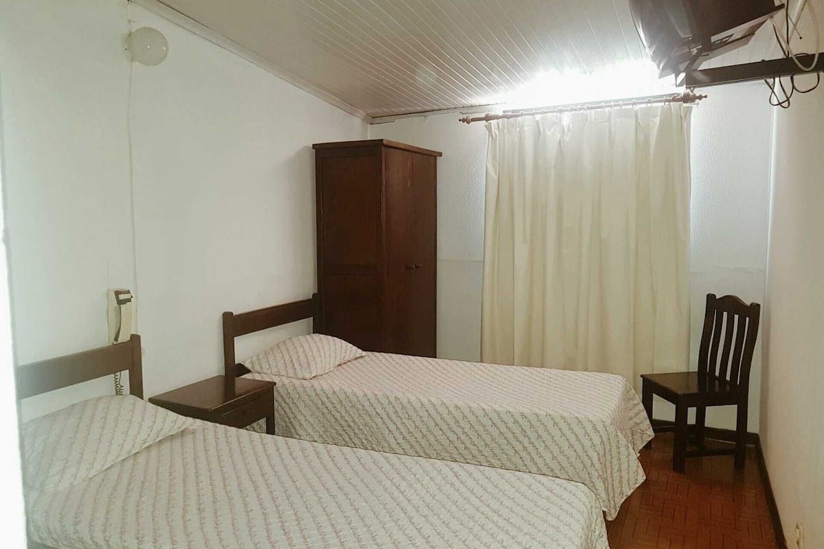 A room with two single beds, a wooden wardrobe, a chair, and a curtain.