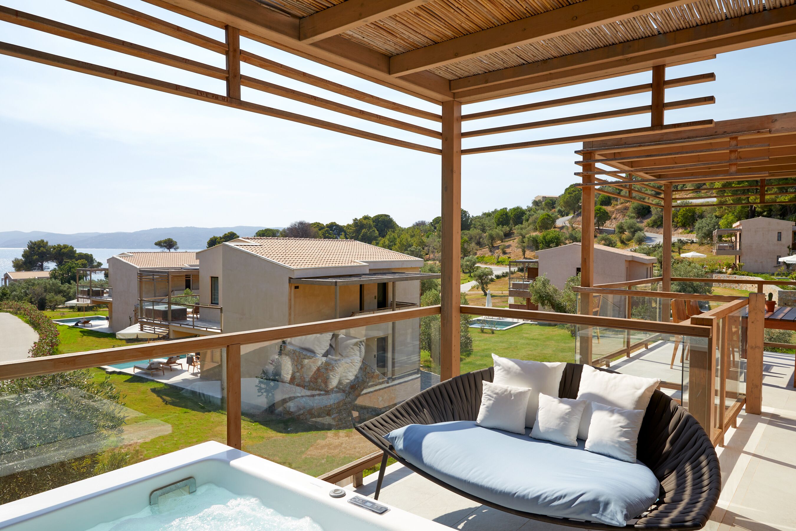 A modern outdoor seating area with a glass balustrade, a hot tub, and a view of the surrounding landscape and buildings.