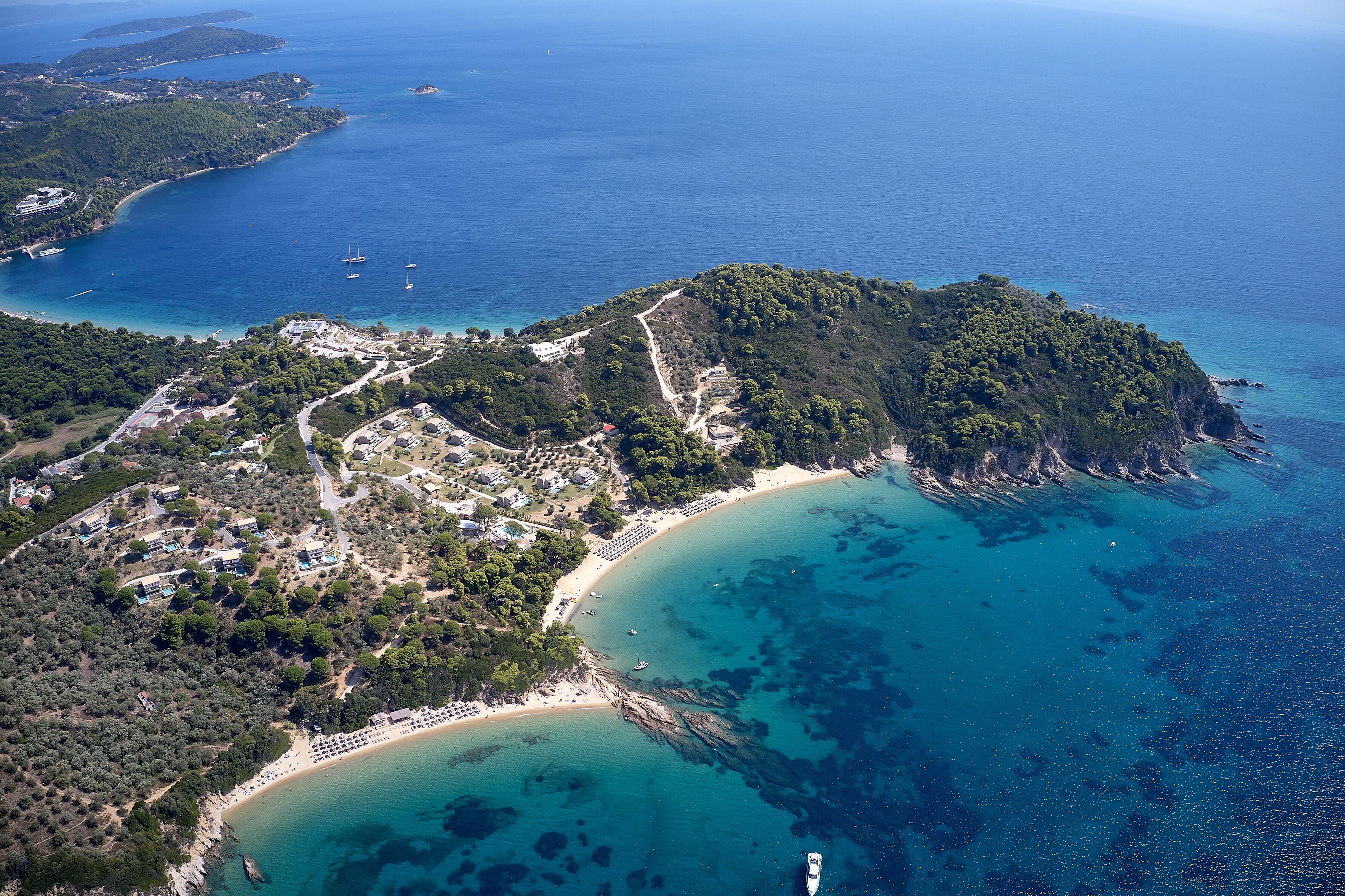 An aerial view of a coastal area with a beach, a small town, and clear blue waters.