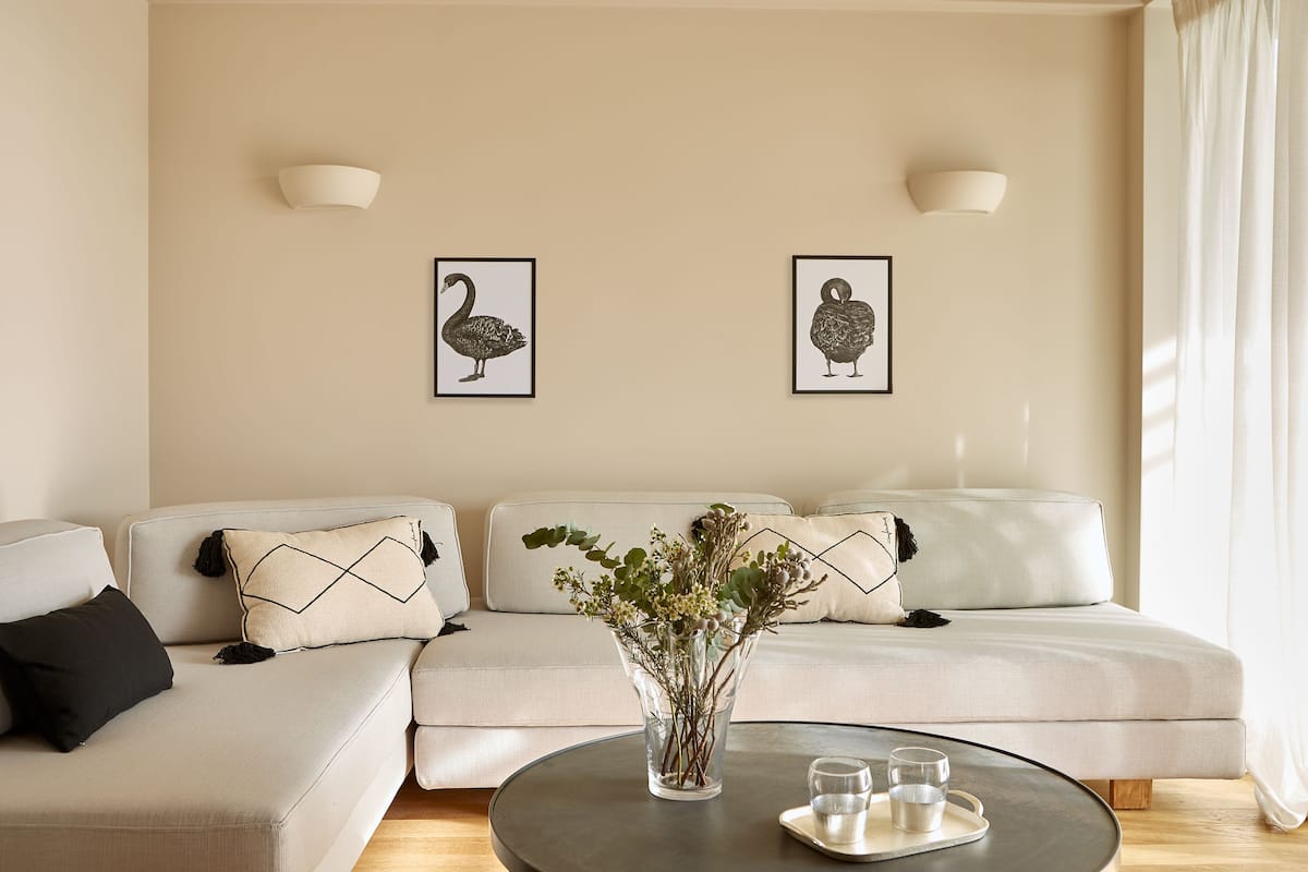 A modern living room with a beige sofa, a glass coffee table, and two wall-mounted light fixtures.