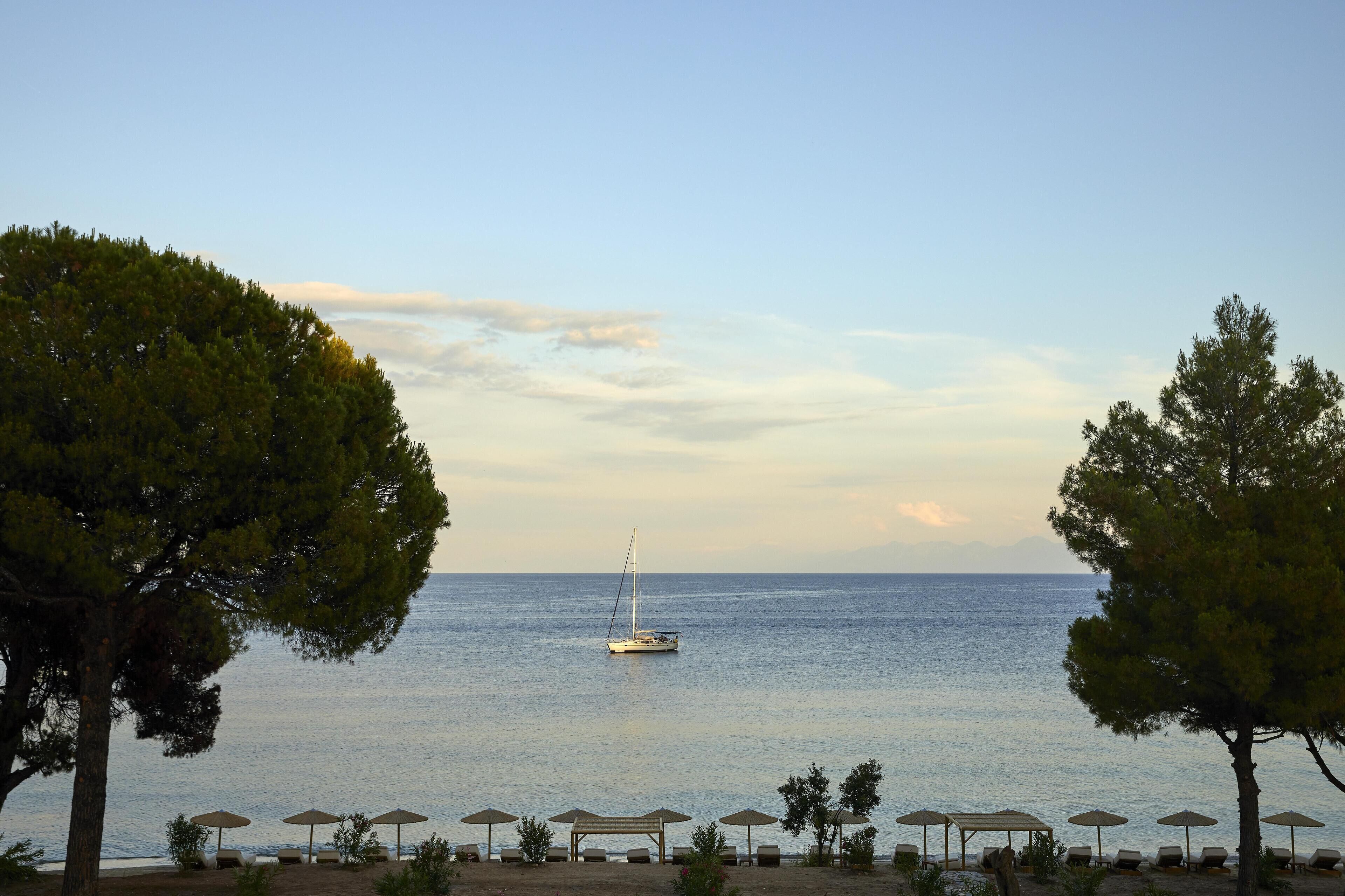 A beach with a sailboat, umbrellas, and lounge chairs.