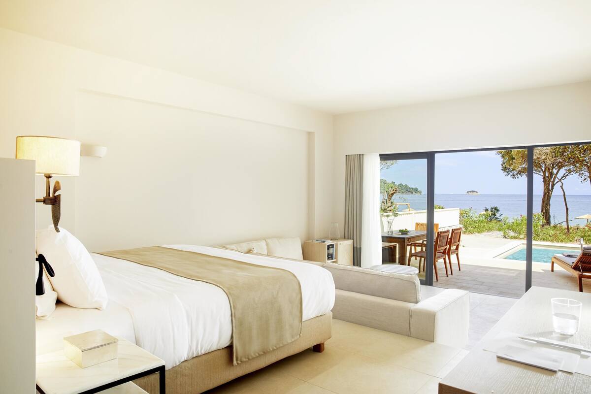 A hotel room with a bed, a bedside table, a desk, and a view of the sea.