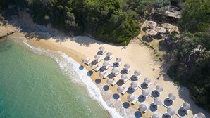 An aerial view of a beach with rows of sun loungers and umbrellas, a rocky cliff, and dense greenery. - ELIVI Skiathos (Skiathos)
