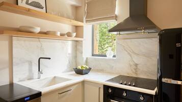 A modern kitchen with a built-in oven, a black refrigerator, and a window with a view of greenery.