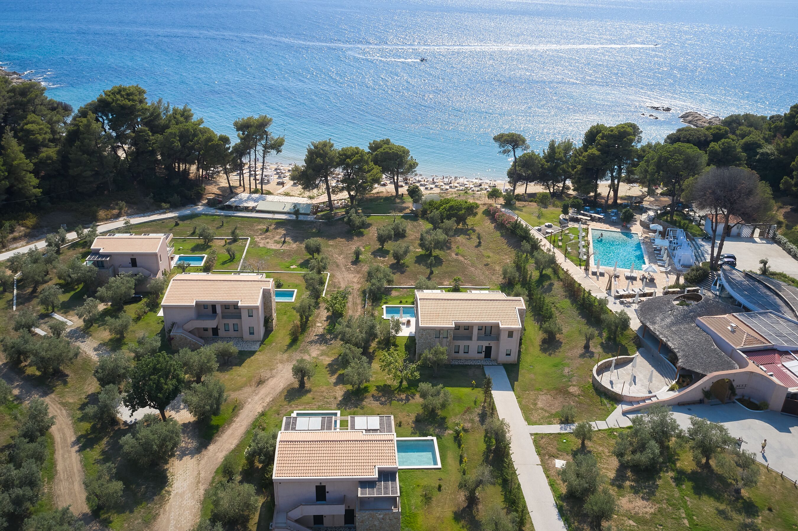 An aerial view of a coastal residential area with multiple houses, a swimming pool, and a beach in the background.