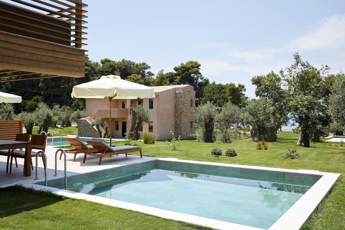 A modern pool area with lounge chairs and umbrellas, surrounded by a well-maintained lawn and trees.