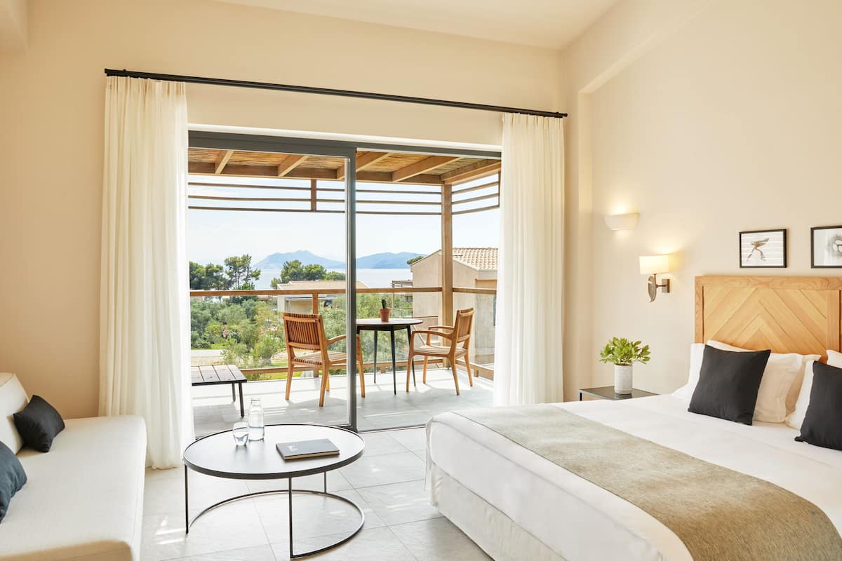 A hotel room with a bed, a small table, a sofa, and a balcony with a table and chairs.