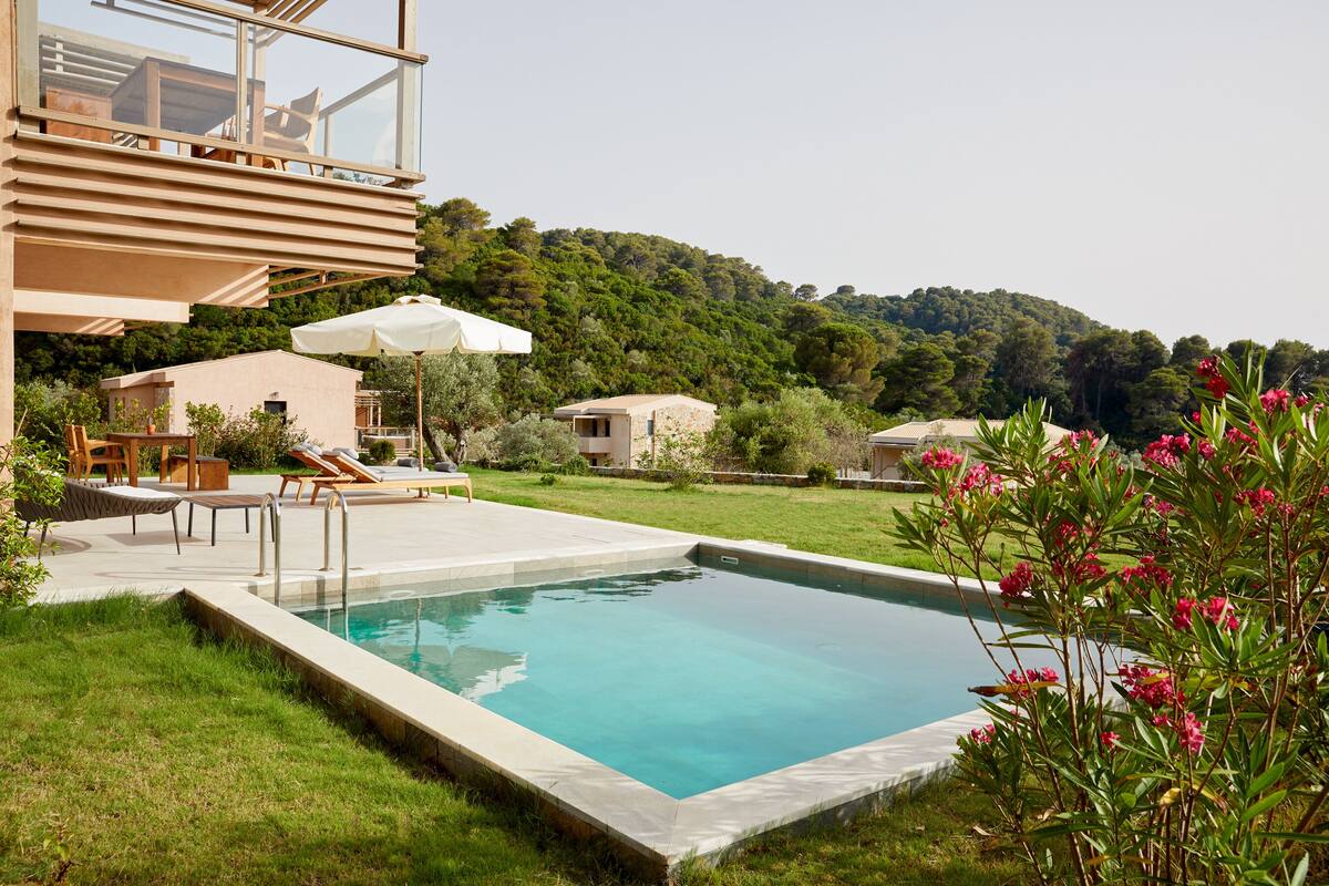 A modern outdoor pool area with a clear view of the surrounding landscape, including a hillside and a building with a glass balcony.