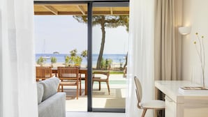 A modern room with a sliding glass door leading to an outdoor area with a pool, wooden furniture, and a view of the sea. - ELIVI Skiathos (Skiathos)