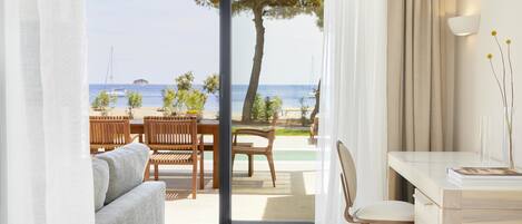 Una habitación moderna con un ventanal corredero que da a un área exterior con piscina, mobiliario de madera y vistas al mar.