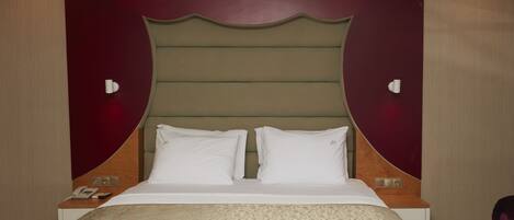 Una habitación de hotel con una cama grande, dos mesitas de noche, un teléfono y una lámpara fijada a la pared.
