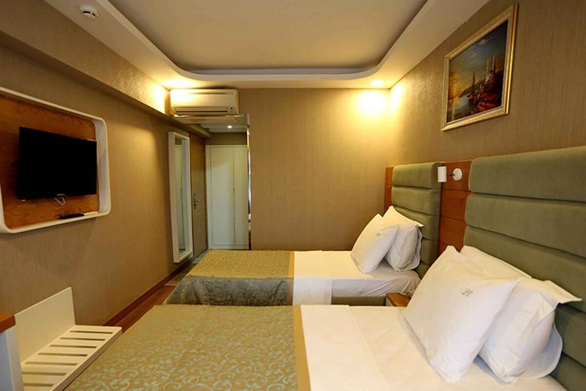 A hotel room with two beds, a television on the wall, and an air conditioning unit.