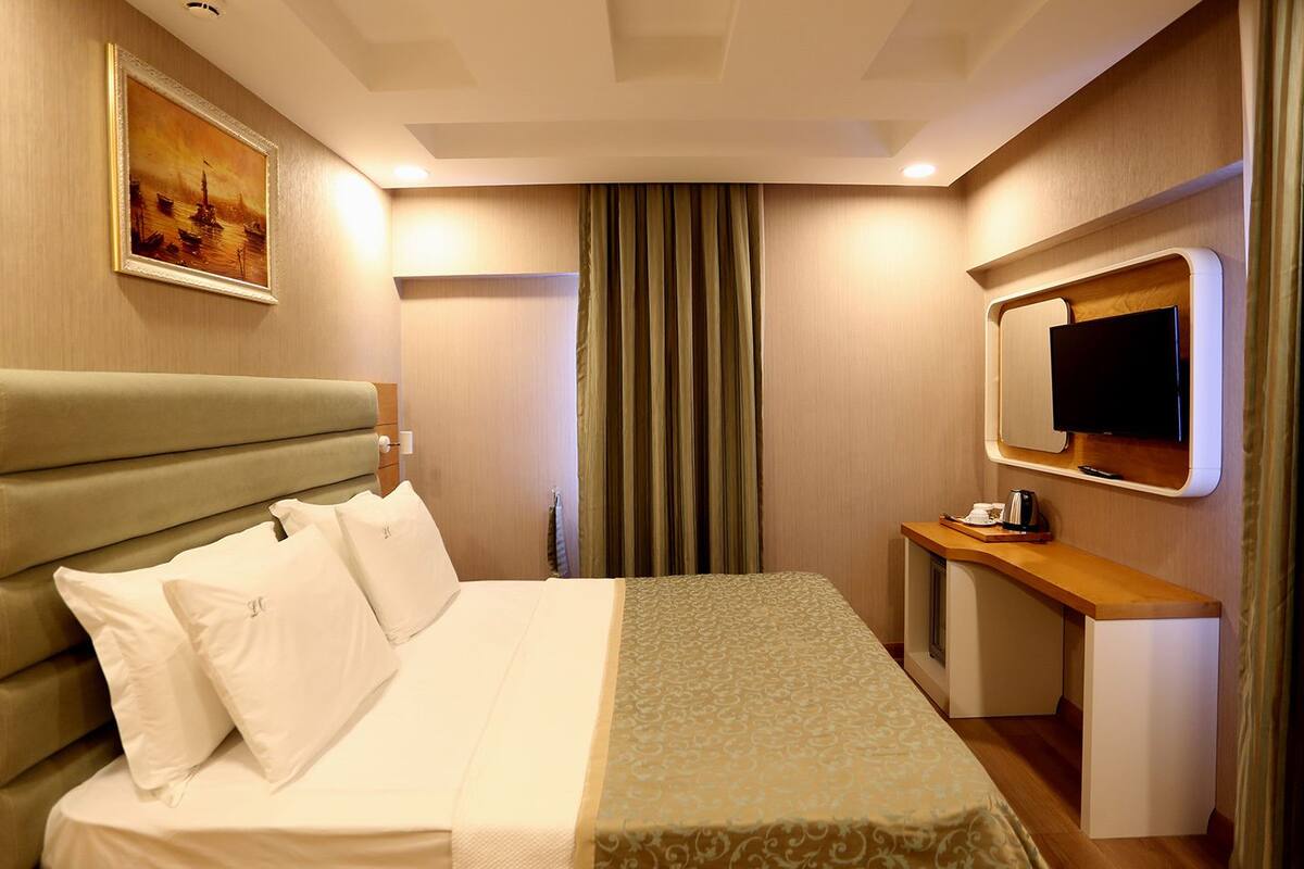 A hotel room with a bed, a desk, a television, and a painting on the wall.