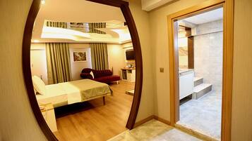 Een moderne hotelkamer met een bed, een rode bank, een bureau en een trap naar een hoger niveau.